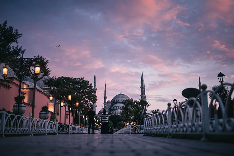 Two people walking toward the Blue Mosque in Istanbul at sunset with pink and purple sky