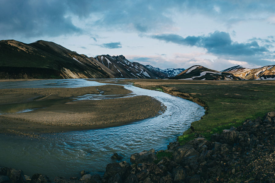 Glacial blue river winding through a rugged mountain valley under moody clouds