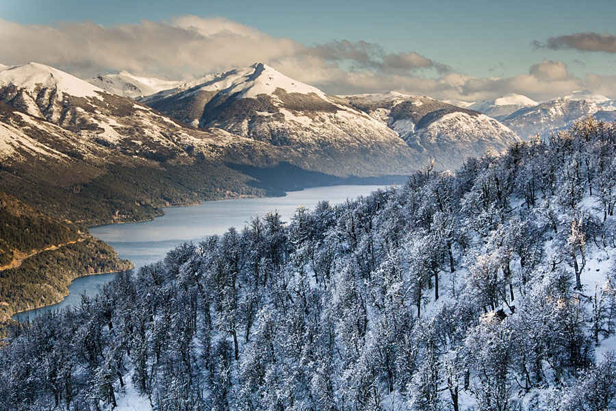 Snow-covered mountains and frosted pine forest above a blue alpine lake in winter