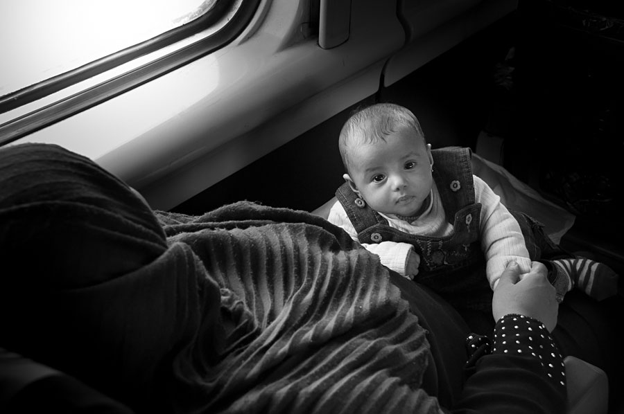 Black and white portrait of a baby in overalls looking at the camera on a train