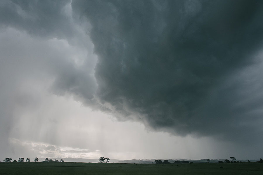 Massive dark storm clouds sweeping across flat green African grassland with scattered trees