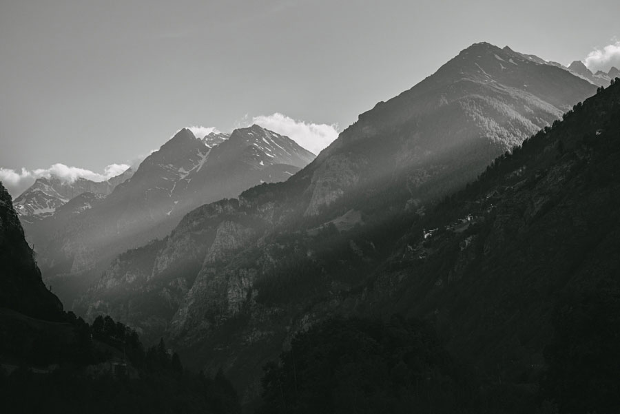 Black and white mountain peaks with light cutting through hazy alpine valleys