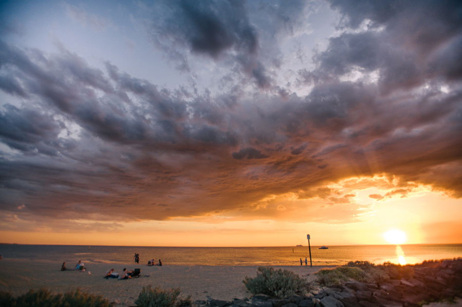 Dramatic golden sunset over a beach with dark storm clouds and scattered beachgoers