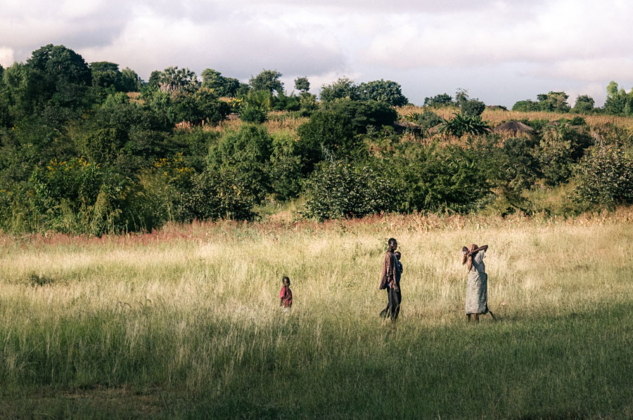 Family of three walking through tall grass in a rural African landscape