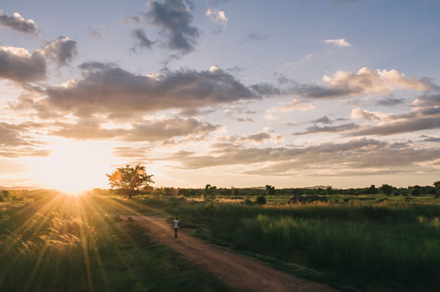Person walking down a dirt road toward a golden sunset in the African countryside