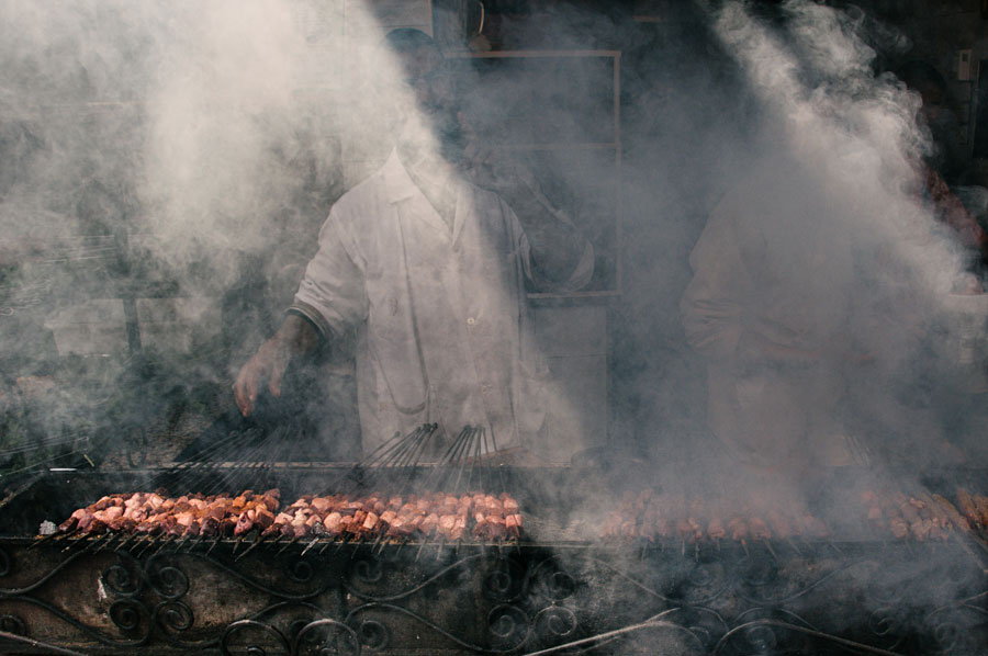 Street food vendor grilling kebab skewers shrouded in thick smoke