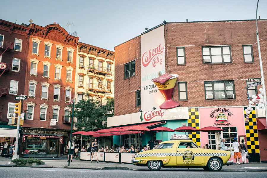 Colorful New York City street corner with a vintage yellow taxi and Caliente Cab signage