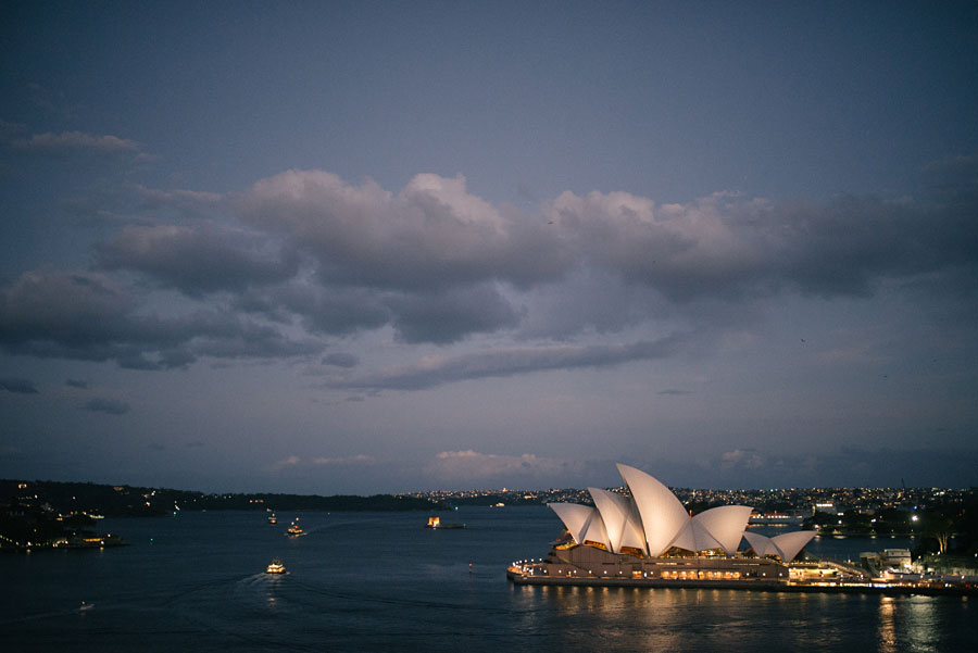 Sydney Opera House illuminated at dusk with boats on the harbour and dramatic clouds