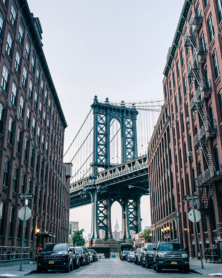 Manhattan Bridge framed between red brick apartment buildings in DUMBO, Brooklyn