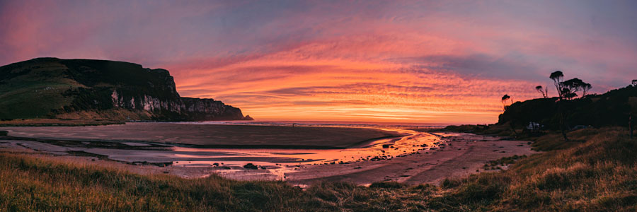 Panoramic coastal sunset with vivid pink and orange sky over a sheltered bay with cliffs