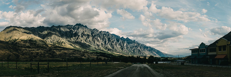 Road leading toward jagged mountain peaks under scattered clouds in New Zealand