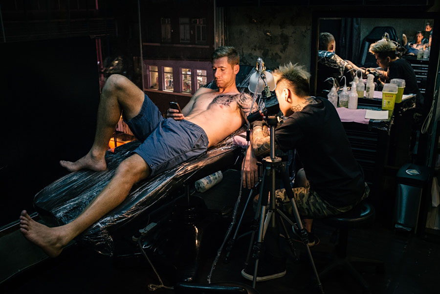 Tattoo artist working on a client in a dimly lit Bangkok tattoo studio