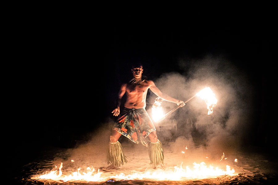 Polynesian fire dancer performing with flaming torches on a sandy beach at night