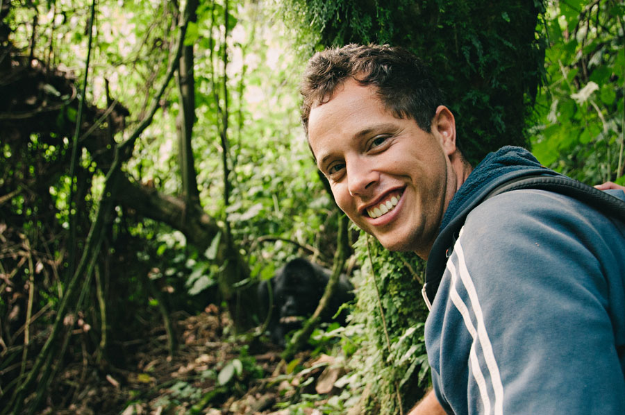 Photographer smiling in the Bwindi jungle with a mountain gorilla visible in the foliage behind him