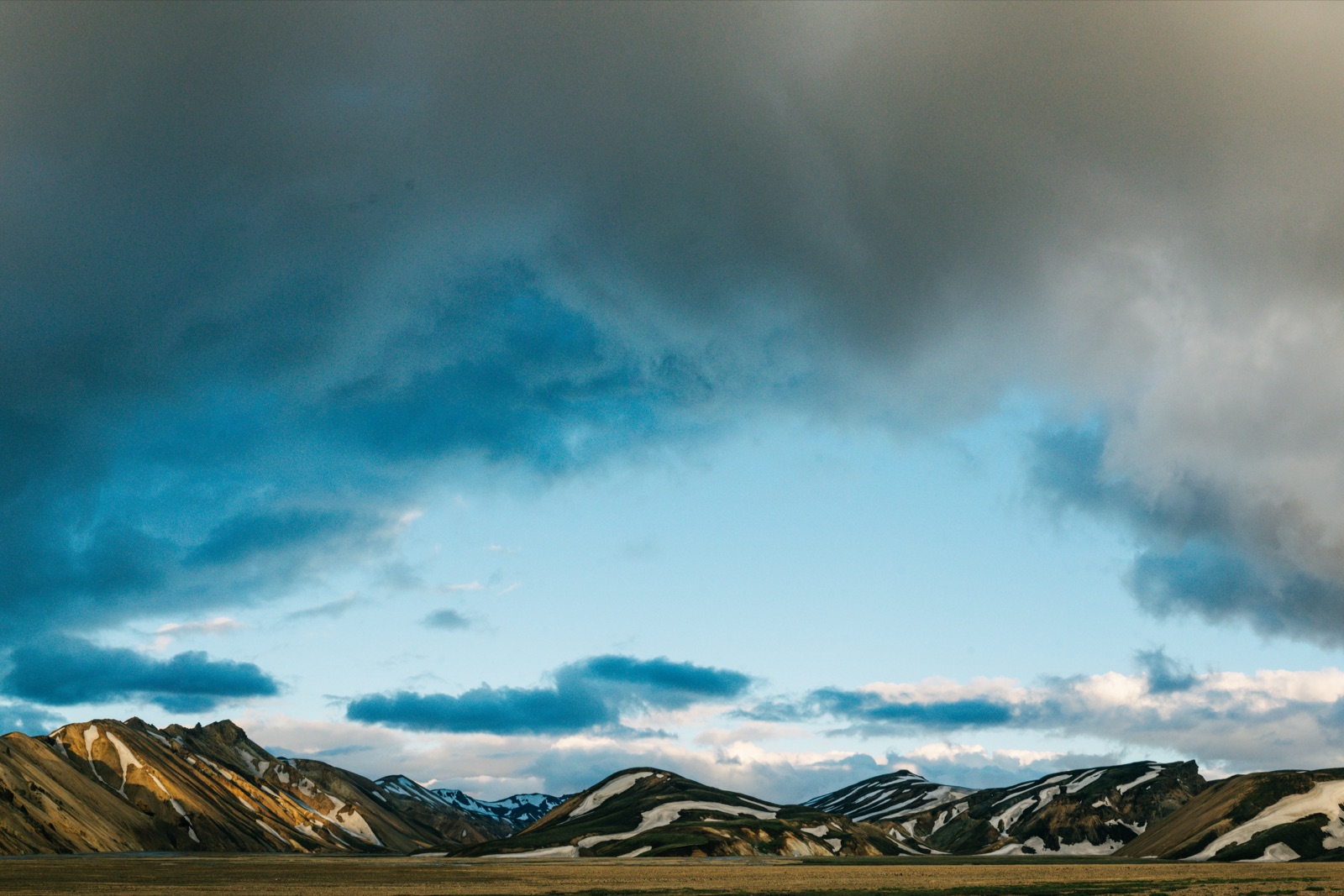 Rhyolite mountains of Landmannalaugar, Iceland under a streak of blue sky breaking through heavy cloud