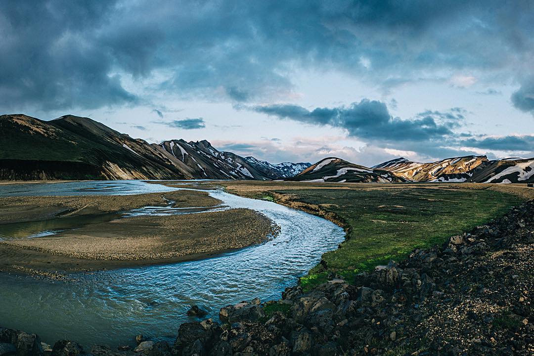 Glacial river winding through the Landmannalaugar highlands with snow-patched mountains under moody skies
