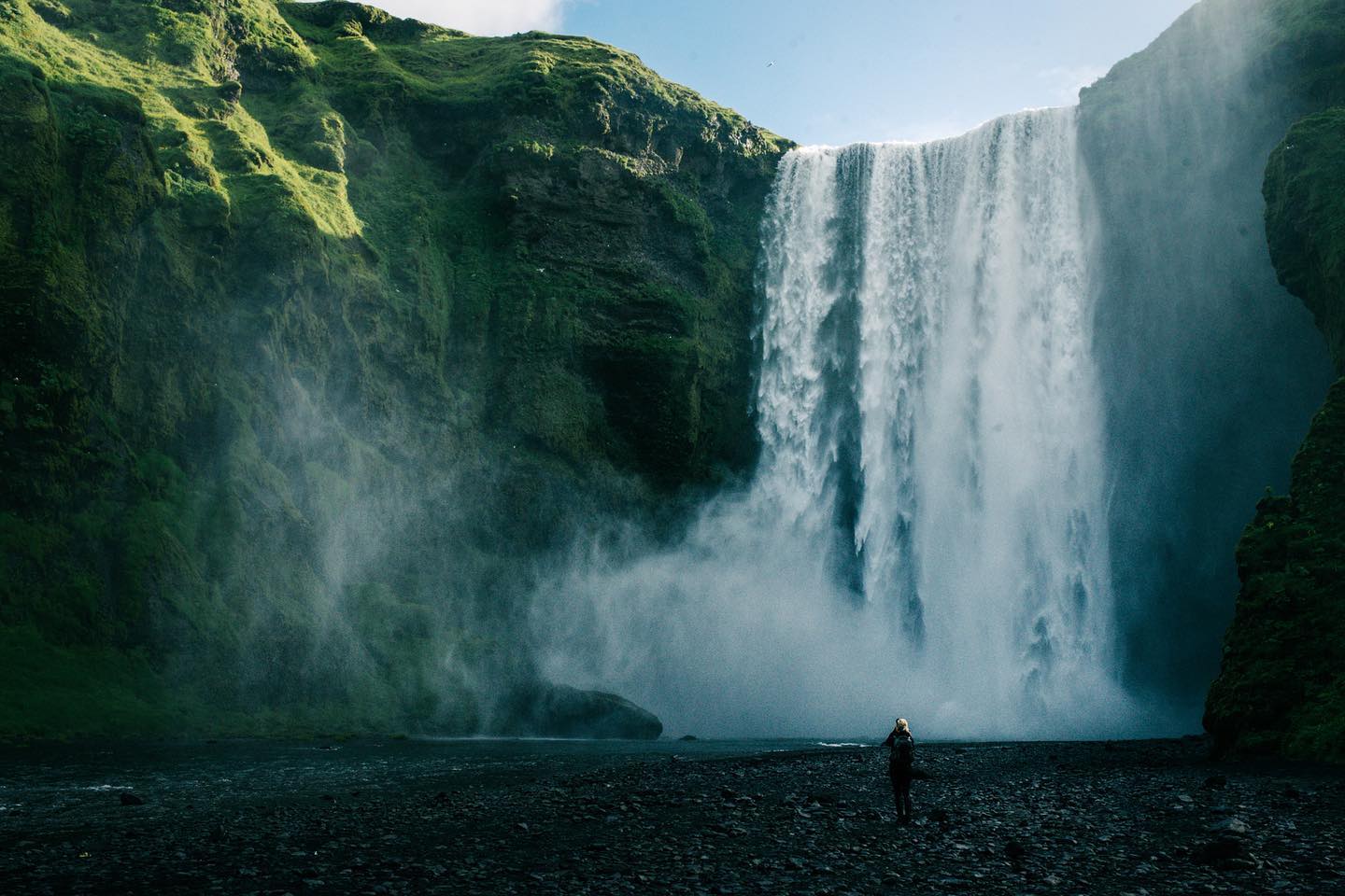 Person standing at the base of Skogafoss waterfall with mist rising from the cascade, southern Iceland