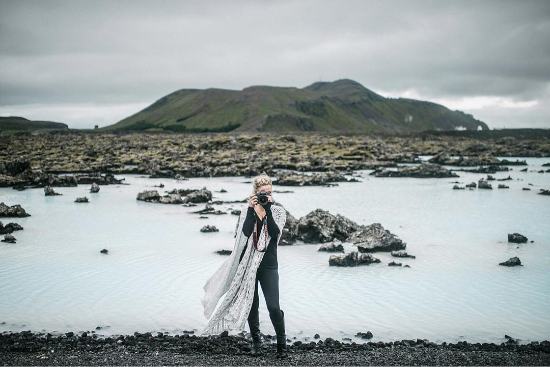 Woman standing in milky blue geothermal water with volcanic mountain rising behind, Iceland
