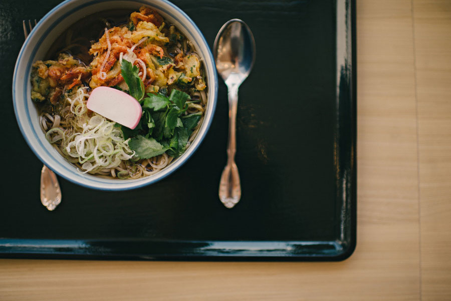Bowl of soba noodles with tempura, kamaboko, and green onion served on a black lacquer tray