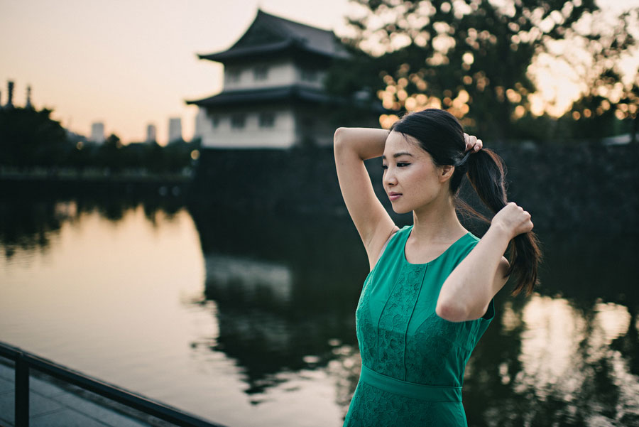 Woman in a green dress tying her hair beside the Imperial Palace moat in Tokyo at sunset