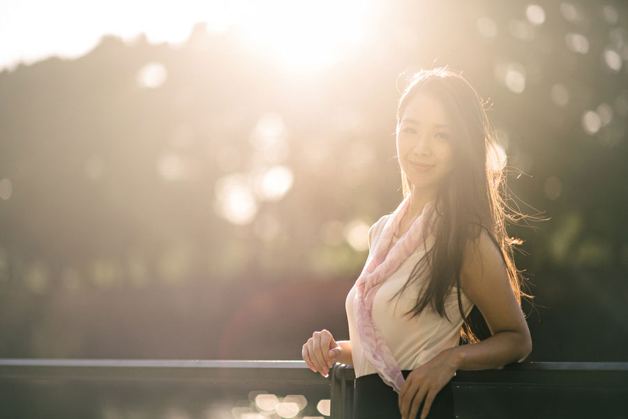 Young woman leaning on a railing with golden hour backlight and bokeh from trees