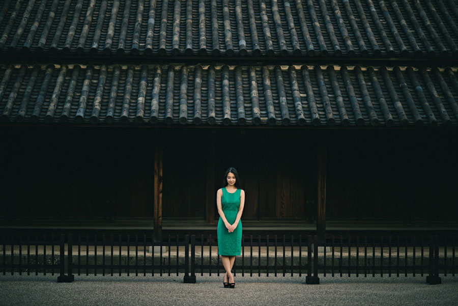 Woman in a green dress standing before a traditional Japanese temple building with tiled roof