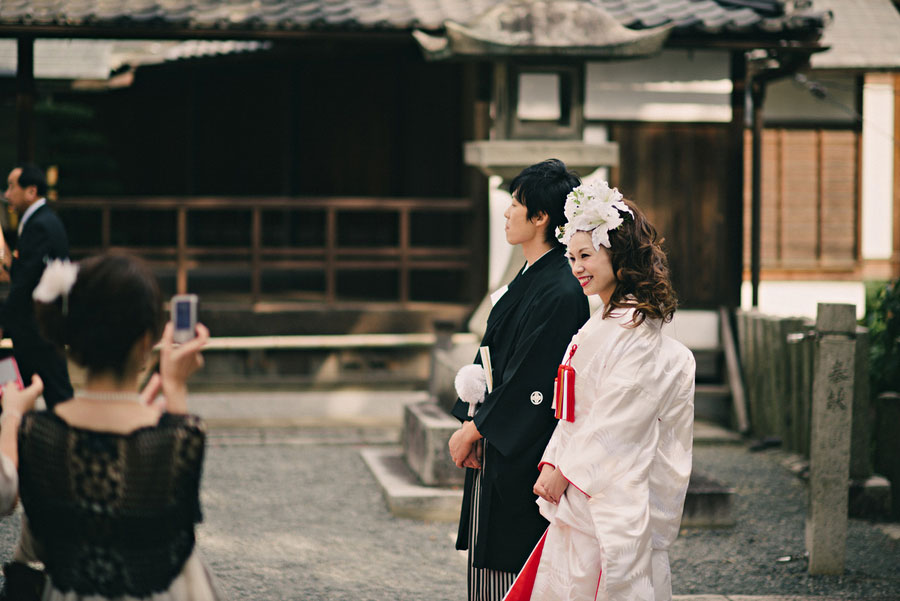 Japanese bride in white shiromuku and groom in black montsuki hakama posing at a shrine