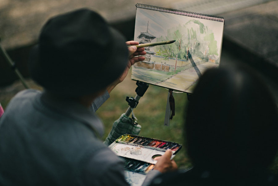 Artist painting a watercolor of a temple pagoda on a portable easel outdoors