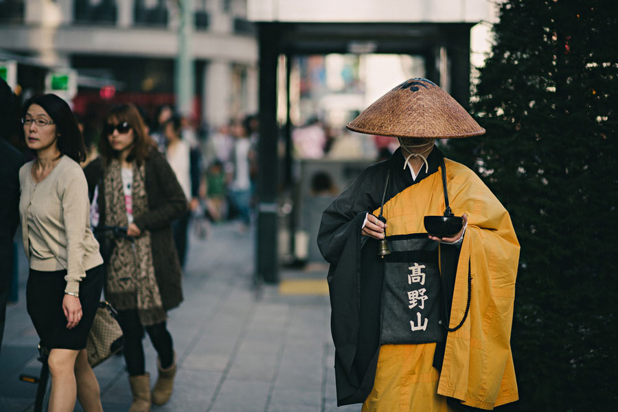 Buddhist monk in saffron and black robes collecting alms on a busy Tokyo sidewalk