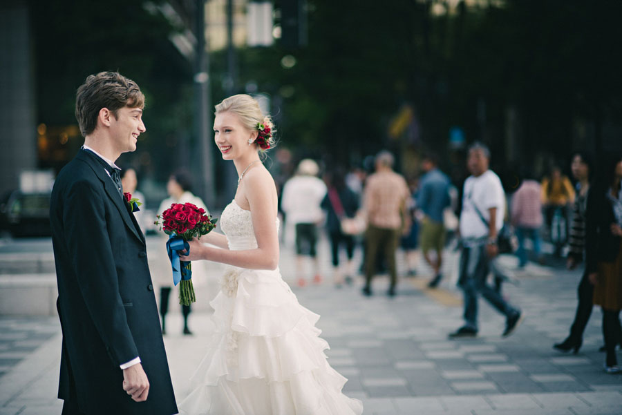 Bride and groom with a red rose bouquet smiling at each other on a busy Tokyo street