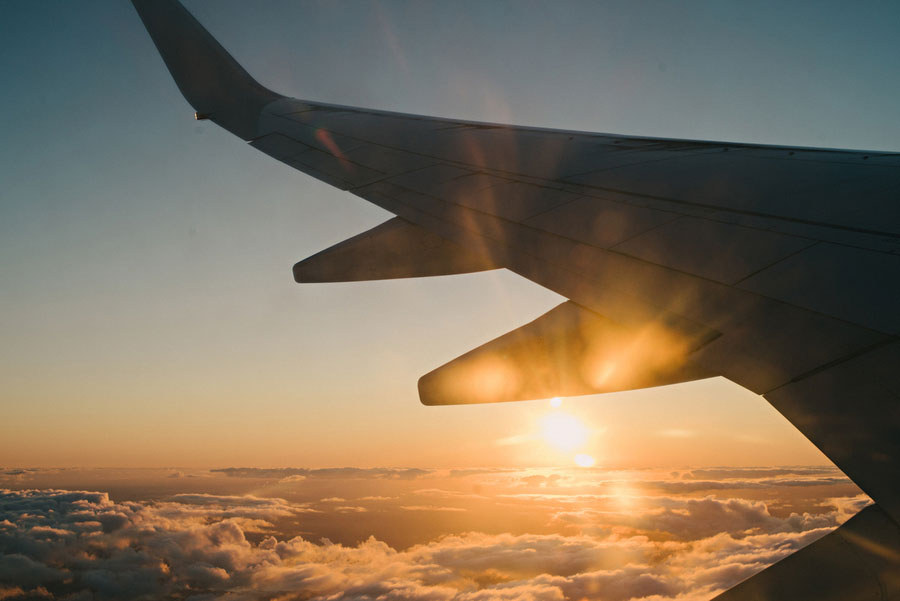 Airplane wing silhouetted against a golden sunset above the clouds