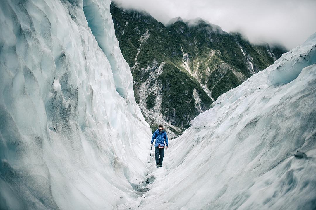 Hiker walking through blue ice formations on Franz Josef Glacier, New Zealand