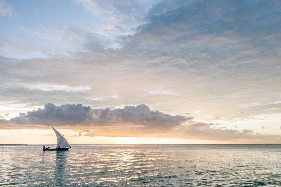 Dhow sailing boat on calm waters at sunset off the coast of Zanzibar, Tanzania