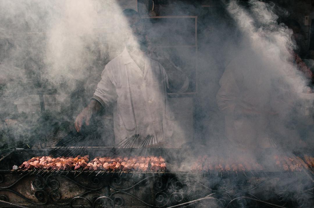 Street food vendor grilling kebab skewers engulfed in smoke in Marrakesh, Morocco